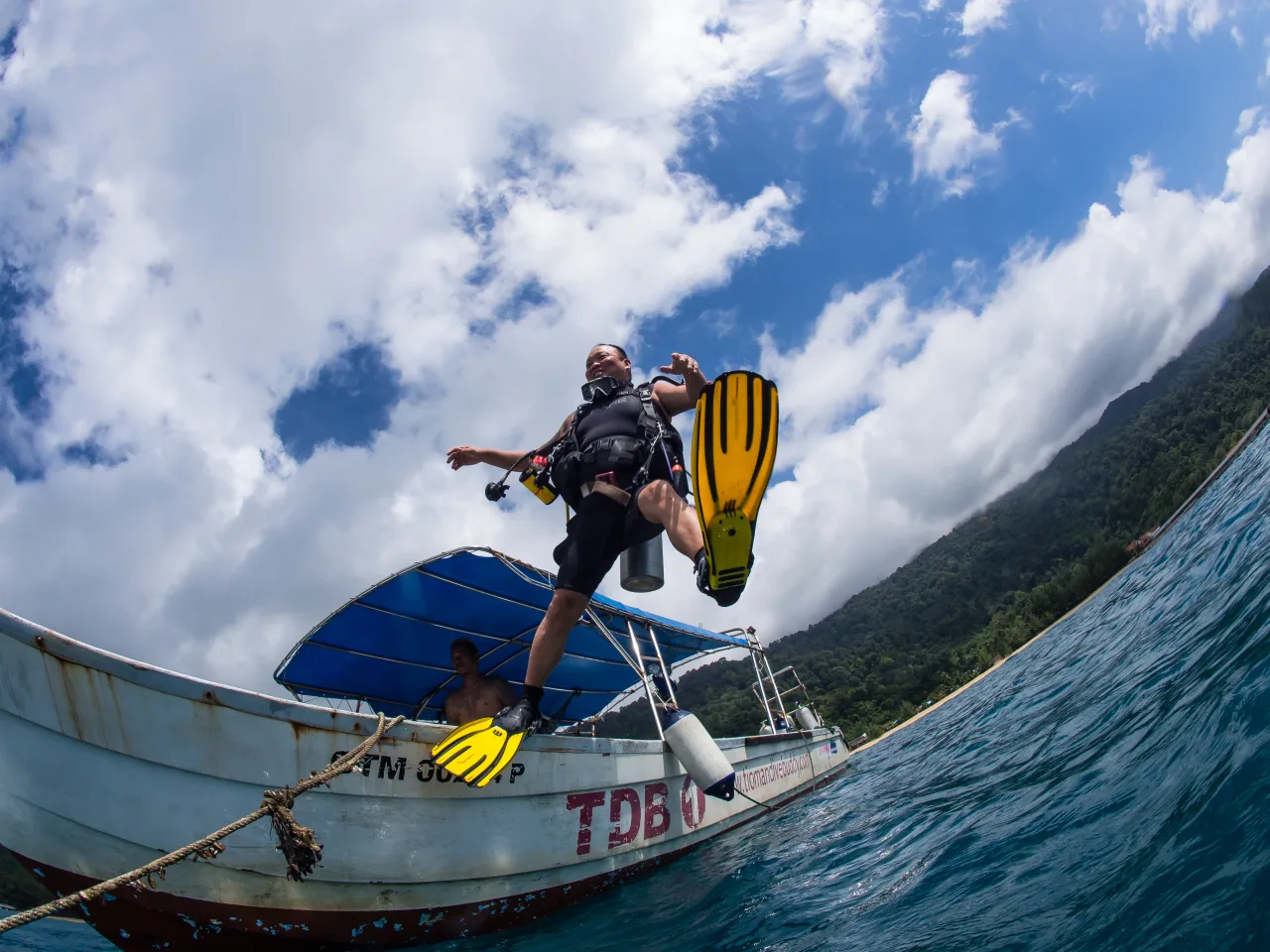 A scuba diver wearing full dive gear stepping from a boat into the sea